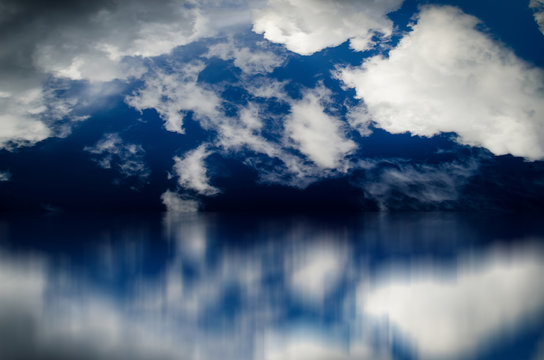 Blue sky. Dramatic clouds over sea. Blurred reflection of sky in water