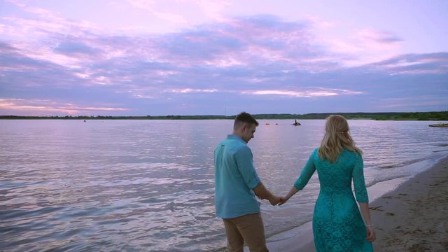 Couple holding hands on beach sunset on honeymoon vacation travel. Happy romantic young lovers, man and woman walking on beautiful beach