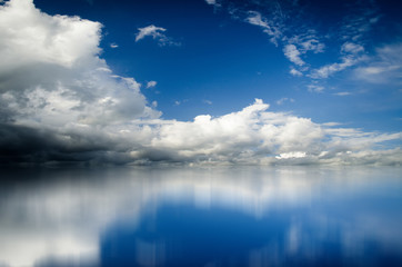 Obraz premium Blue sky. Dramatic clouds over sea. Blurred reflection of sky in water