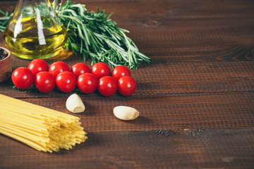 Spaghetti, tomatoes cherry, olive oil, herb and spices on old brown wooden background