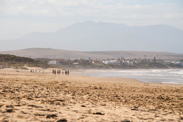 Fototapeta na wymiar A group of people walking along a beach in Mossel Bay, South Africa