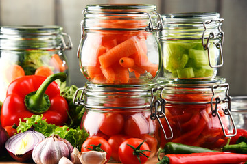Fototapeta na wymiar Jars with marinated food and raw vegetables on cutting board