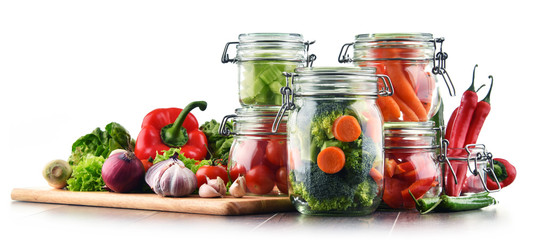 Jars with marinated food and raw vegetables isolated on white