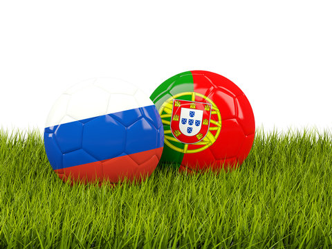 Two footballs with flags of Russia and Portugal on green grass