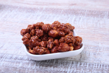 Sugared Hazelnuts in a white bowl on a wooden background. Hazelnuts in sugar glaze. Selective focus.