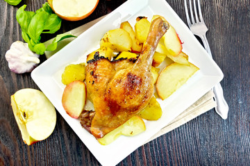 Duck leg with apple and basil in plate on board top
