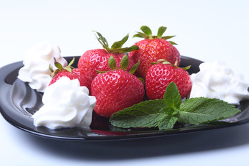 Fresh strawberries with whipped cream and mint leaves on a black plate. Selective focus.