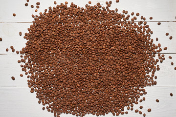 Roasted brown coffee beans scattered on white wooden table, top view background