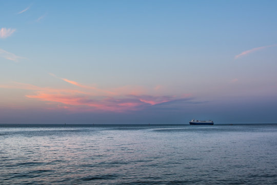 Big vessel standing on the horizon under pink sunset cloud. Roadstead of Gdansk port.