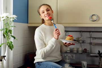 Happy young woman eating breakfast with pancakes on kitchen, healthy lifestyle