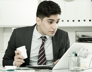 Young manager is working at a computer and drinking coffee