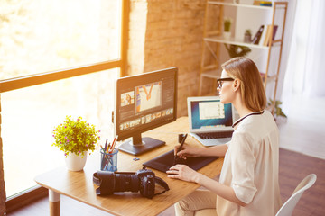 Professional successful photographer sitting at the table and using digital graphic tablet for...