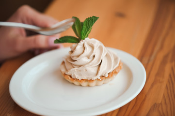 Woman eating a cake of cottage cheese in a ceramic plate with a spoon on a wooden table