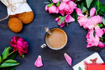 Obraz na płótnie Canvas The concept with morning coffee in a romantic style on the black wooden background. Peonies flowers and petals, cookies, mug with coffee . Top view, flat lay. Selective focus
