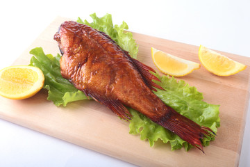 Smoked fish and lemon on green lettuce leaves on Wooden cutting board isolated on white background.