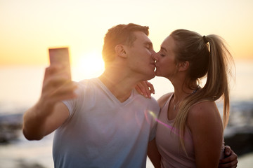 Couple on a date takes a kissing selfie with sunset