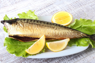 Smoked mackerele and lemon on green lettuce leaves on Wooden cutting board isolated on white background.