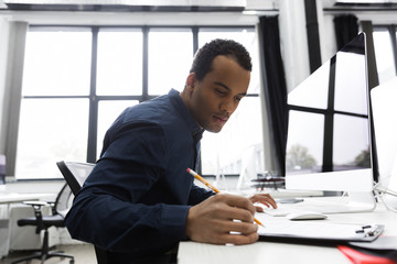 Afro american businessman making notes while sitting at his desk