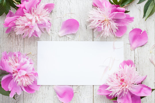 Mockup- flowers, peonies on a wooden table, white card. Woman's desk.