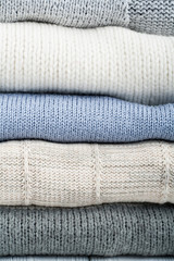 Knitted wool sweaters. Pile of knitted winter clothes on wooden background, sweaters, knitwear, space for text.