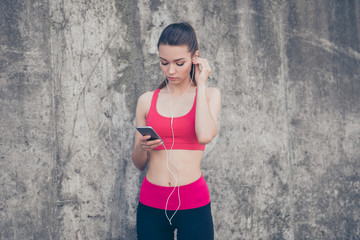 Attractive fit sportgirl is putting music on her smartphone before work out. She is outdoors on a summer day, wearing stylish sport wear