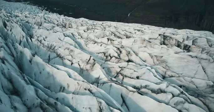 Copter fly over the ice ridge in Iceland. Close-up aerial view of white glacier Vatnajokull with black ash.