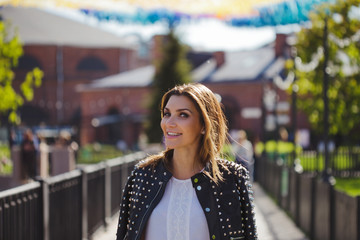 Stylish woman walks around the city. In a leather jacket on her shoulders, looks at you a beautiful smile