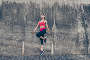 Fitness sport woman in fashion sport wear is jumping in the city street on the grey concrete background. Outdoors sports clothing and shoes, urban style