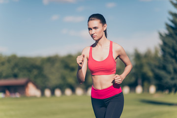 Healthy sunny mood. Young lady athlete is running outdoors, training for marathon run. Beautiful fitness model, in fasionable sports outfit, so focused, fit and fast!