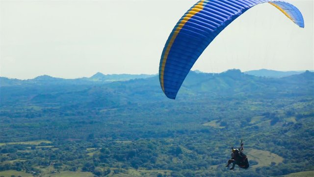 Super slow motion. Two People ride Paramotor paraglide paraplane flying in the sky with mountains midday sunny. Blue clouds.