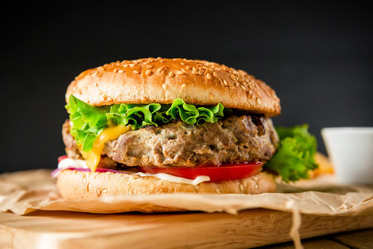 Classic hamburger with tasty beef, tomato, salad and cheese on dark background. American food