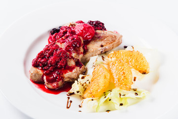 Foie gras in a sauce of wild berries with a lettuce leaf and orange on a white plate on a light background (close)