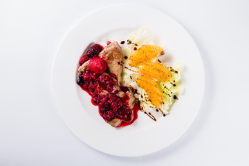 Foie gras in a sauce of wild berries with a lettuce leaf and orange on a white plate on a light background (top view close)