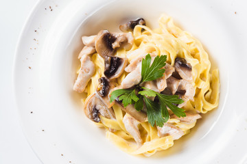 Pasta with chicken and mushrooms on a round white plate on a light background (close top view)