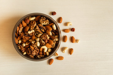 Mixed nuts in a metal brown bowl on a white wooden background.
