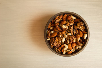 Mixed nuts in a metal bowl on a white wooden background.