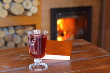 A mug of tea and a book are on a wooden table in front of the fireplace.