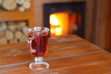 A glass of tea standing on the wooden table in front of the fireplace.