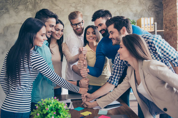 Businesspeople putting their fists on top of each other on the desktop in nice light workstation, wearing casual clothes. Conception of successful team-building