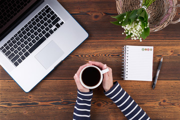 Woman with laptop on rough wooden table, working blogging relaxed with cup of coffee and flowers, top view