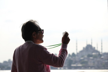 An old Japanese tourist is taking photos of Bosphorus in front of Sultan Ahmed Mosque as known as...