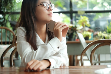 asia woman holding mobile phone sitting and waiting for someone in coffee cafe. image for business,people,portrait,mobile and technology concept