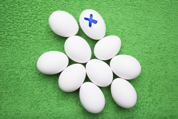 Ten white chicken eggs lie on a grassy-green background, one egg is marked with the sign of X
