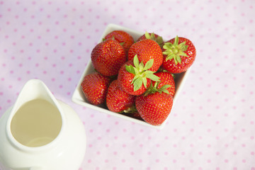 Strawberries in a white angled bowl on a pink dotted tablecloth in bird's eye view