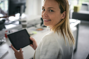 Business woman in office. Woman using digital tablet and looking at camera.