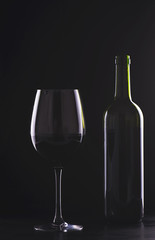 Cup and empty wine bottle on black background.