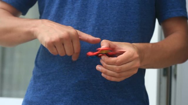 Multicolored, red-yellow-blue hand spinner, or fidgeting spinner, rotating on man's hand.