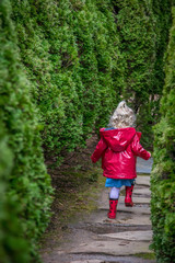 Obraz premium Small girl in raincoat running down a garden path
