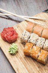 Set of sushi rolls with salmon, black and white sesame, red caviar, ginger and wasabi, sticks for sushi on a light bamboo board