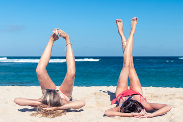 Two happy sexy women friends sunbathing on the tropical beach of Bali island, Nusa Dua, Indonesia.